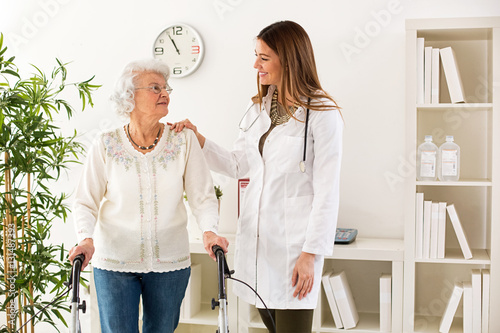 Beautiful young doctor helping senior woman walking with a walke