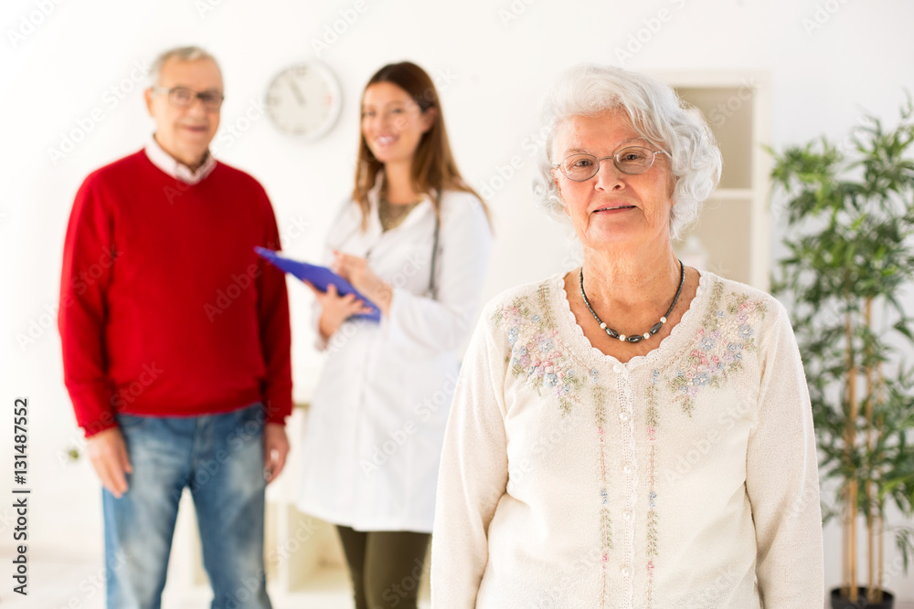 Senior woman smiling with her husband and doctor in background Senior woman smiling with her husband and doctor in background