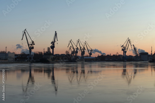 Billede på lærred Silhouettes of of portal cranes reflection on the water