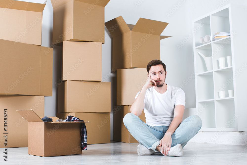 Young man thought sitting on the floor. Moving in house.