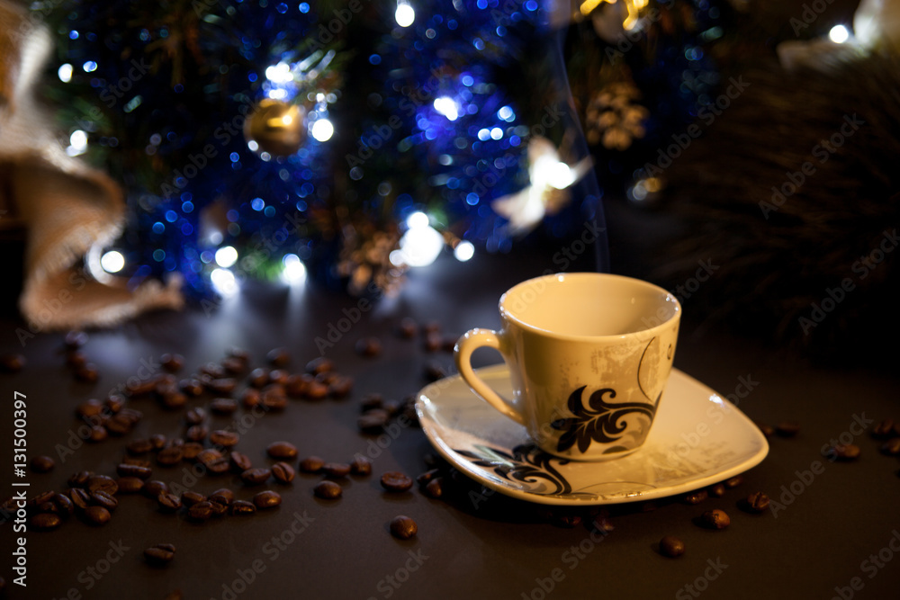 Cup of coffee under the Christmas tree. Coffee beans and hot espresso. Blur light on background. Cup of coffee under the Christmas tree. Coffee beans and hot espresso. Blur light on background.