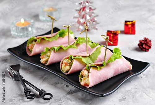 Traditional Russian Christmas salad of boiled potatoes, carrots, eggs, pickled cucumbers, canned peas and mayonnaise in a slice of ham.