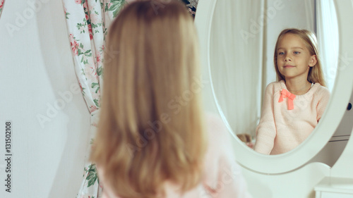 Fashionable little lady combing her hair and looking in the mirror