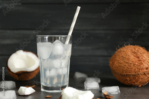 Glass of coconut water and fresh nut on dark wooden background