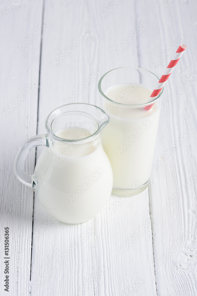Glass of milk with stripped red paper straw and jug of milk on white wooden table still life Glass of milk with stripped red paper straw and jug of milk on white wooden table still life