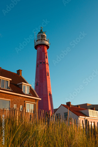 Lighthouse on the Netherlands coast among rural houses, vintage fence and grass
