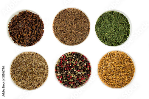 Herbs and seasonings - dried clove, cumin, parsley, coriander, peppercorns and mustard seeds in a transparent dish isolated on white background.