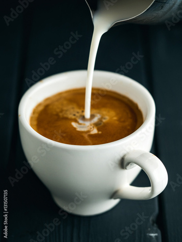Milk pouring into cup of coffee