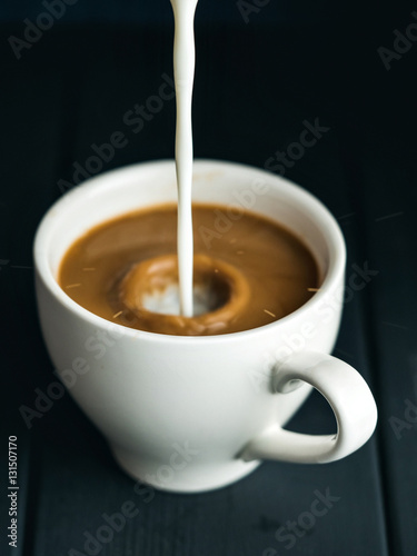 Milk pouring into cup of coffee
