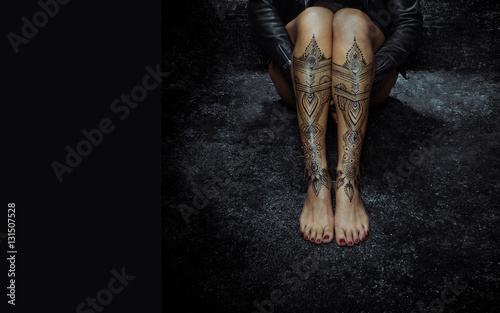 Closeup woman legs with henna tattoo over black stone floor photo