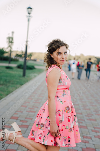 Beautiful brunette girl posing in pink dress outside near tropical plants