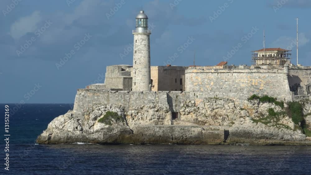 View on huge stone lighthouse into sea bay which is placed in fortress at downtown of Havana. People are walking by seafront. View on huge stone lighthouse into sea bay which is placed in fortress at downtown of Havana. People are walking by seafront.