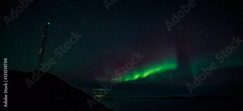 Radio tower on the hill and northern lights over the fjord in th