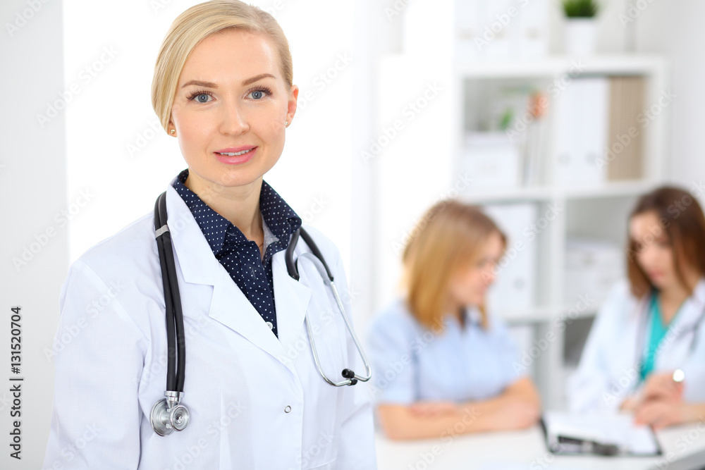 Female doctor smiling on the background with patient and his physician in hospital Female doctor smiling on the background with patient and his physician in hospital