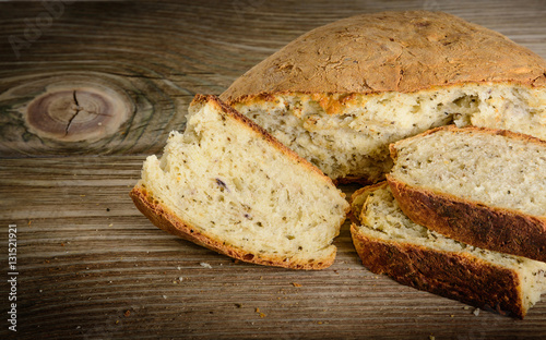 Sliced loaf of homemade bread made with herbs and spices on wooden background.