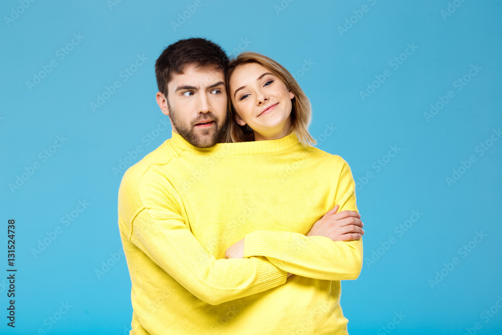 Fototapeta premium Couple in yellow sweater posing with crossed arms over blue background.