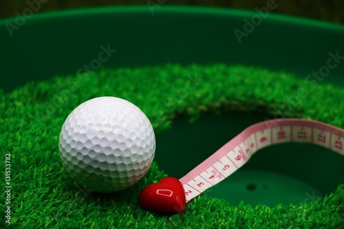 golf ball with red heart shape is on green grass