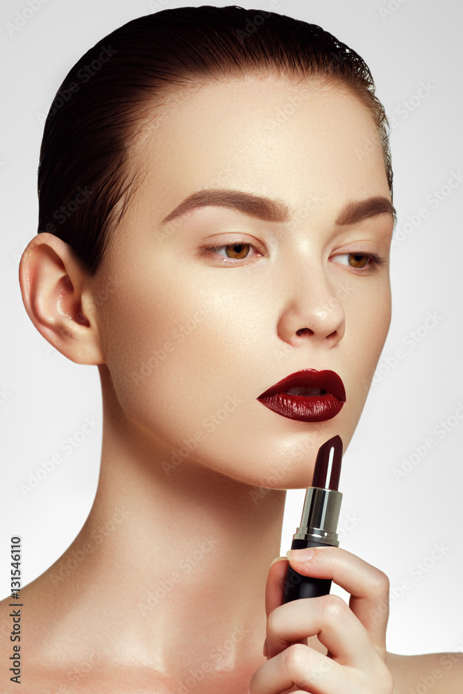 Fototapeta premium Fashion and beauty. Beautiful young woman with wine lipstick. Brunette model with dark red colored pomade. Beautiful model girl applying lipstick