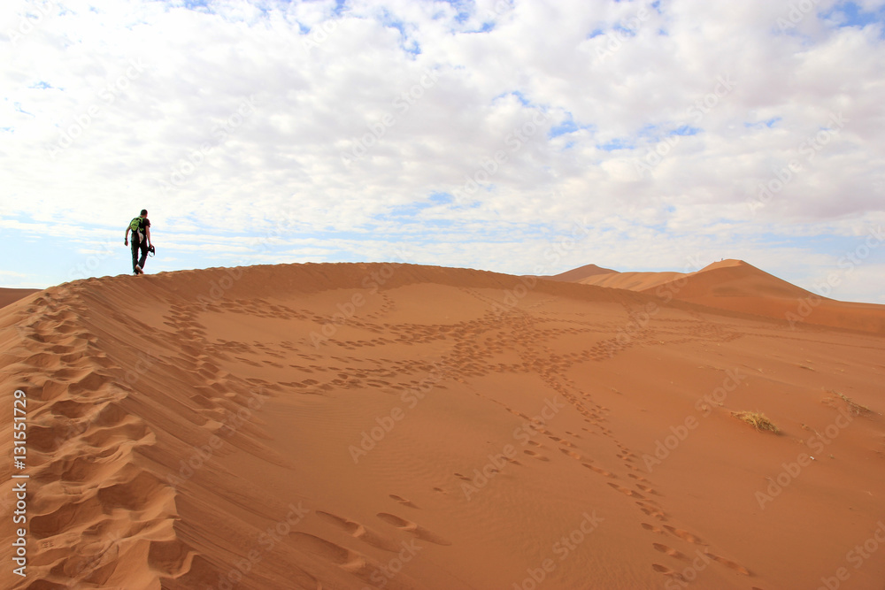 Tourist climbing a dune in the Sossusvlei desert, Namibia Tourist climbing a dune in the Sossusvlei desert, Namibia