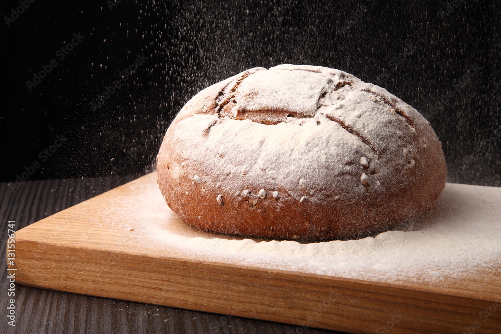bread/ bread, flour sprinkled on an oak board on a dark background bread/ bread, flour sprinkled on an oak board on a dark background