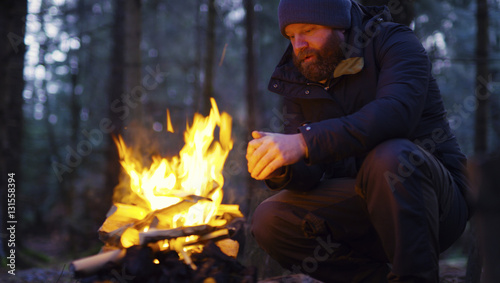 Man warms himself at camp fire in the forest photo