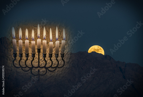 Low key composite image with menorah with glitter lights of burning candles and rise of moon above mountains photo