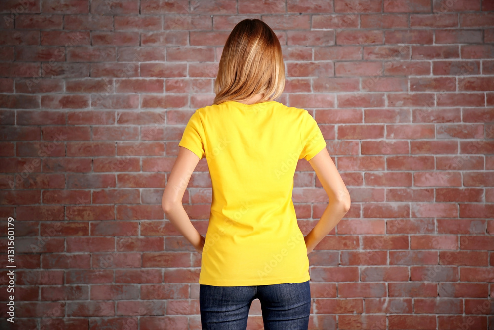 Young woman in blank yellow t-shirt standing against brick wall Young woman in blank yellow t-shirt standing against brick wall