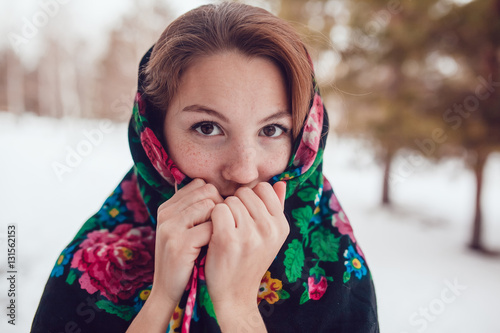 Russian beauty woman with red hair and freckles in the national scarf stands on a background of trees. photo