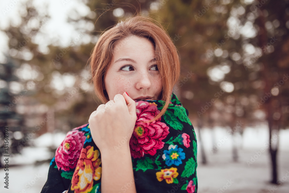 Russian beauty woman with red hair and freckles in the national scarf stands on a background of trees. Russian beauty woman with red hair and freckles in the national scarf stands on a background of trees.