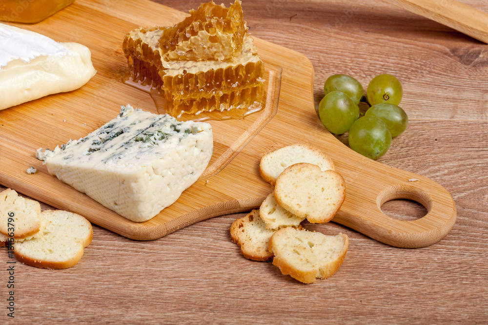 Fototapeta premium Honey, white cheese and other cheese with grape on wooden backgr