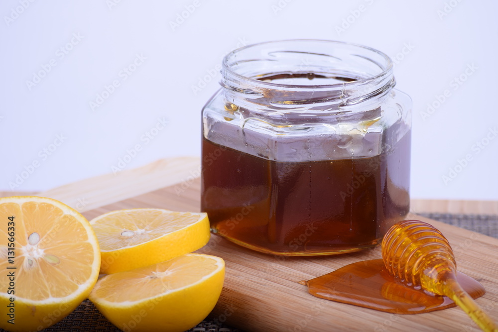 Honey in a jar and lemon served on a wooden board Honey in a jar and lemon served on a wooden board