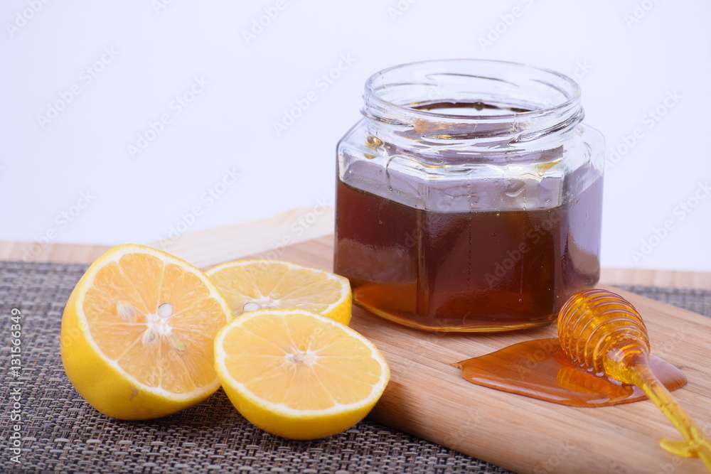 Honey in a jar and lemon served on a wooden board Honey in a jar and lemon served on a wooden board