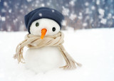 Small snowman in a cap and a scarf on snow in the winter against the background of trees. Festive background with a lovely snowman. Christmas Card, copy space