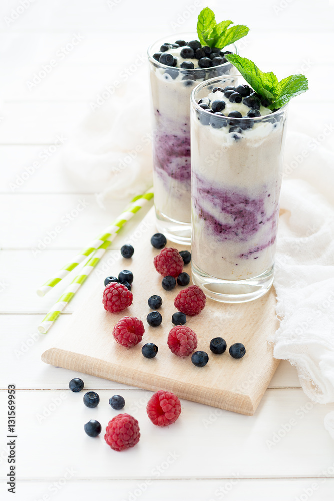 Two glasses with fresh blueberry smoothie decorated berries and mint leaves on white wooden background. Selective focus