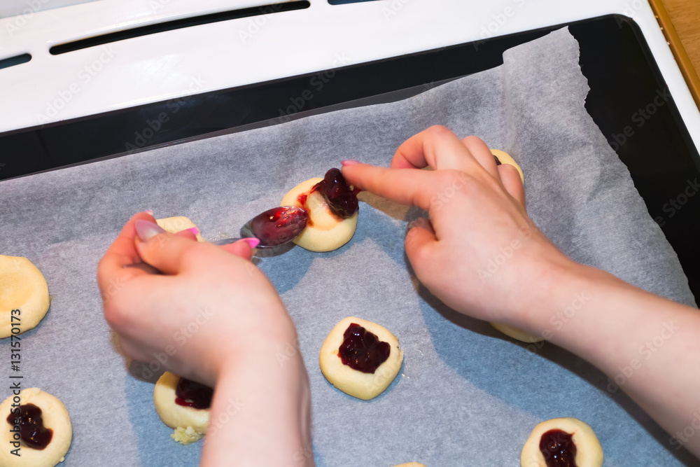 Young woman filling unbaked cookies with jelly jam.