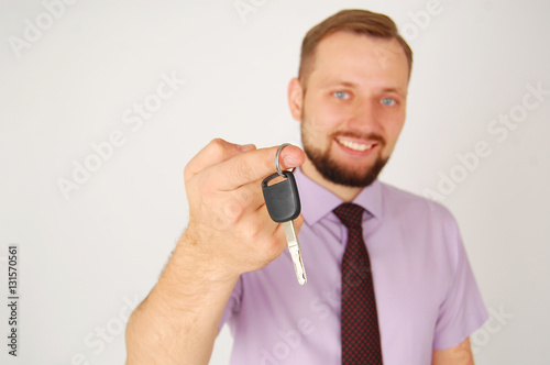 Young handsome man is glad about buying new car. Close up portrait of caucasian guy who holds key from auto.