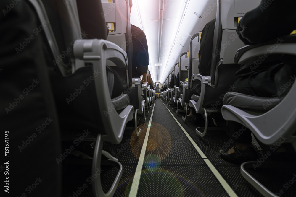 Fototapeta premium Inside the airplane : Modern interior of aircraft. Black seats inside airplane with flare light. Symmetric vanishing row of seats inside air transport. Economy class of flight.