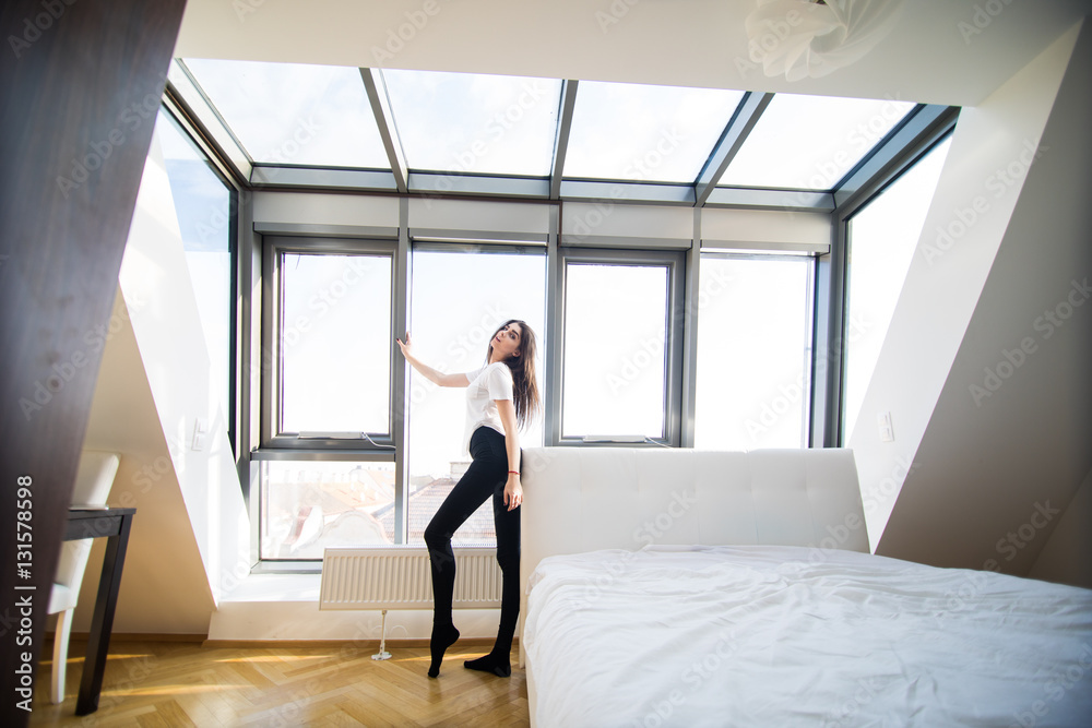 Woman standing near the window while stretching near bed Woman standing near the window while stretching near bed