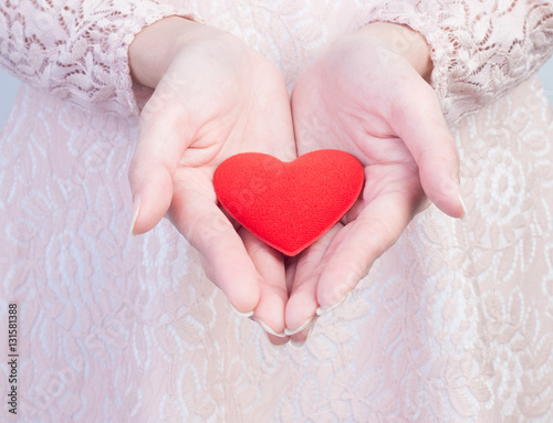 Close up of woman in vintage dress pink color cupped hands showing red heart .