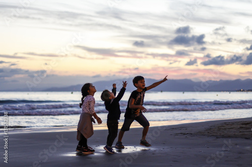 Silhouette of three kids playing on the beach at sunset.
