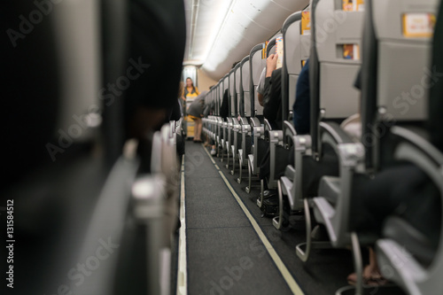 Inside the airplane : Modern interior of aircraft. Black seats inside airplane with flare light. Symmetric vanishing row of seats inside air transport. Economy class of flight.