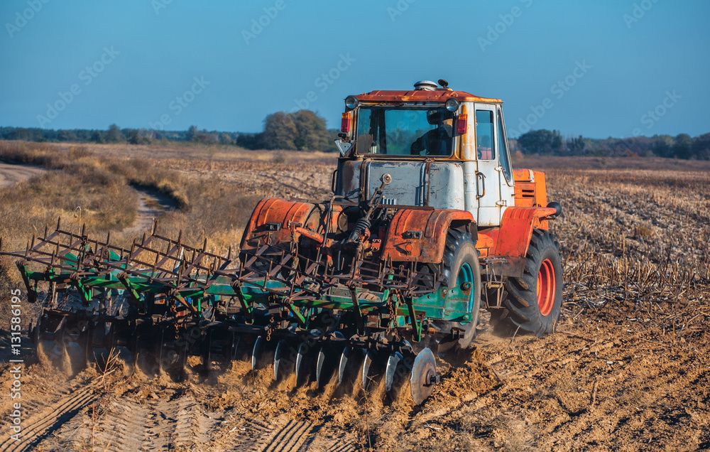 Obraz premium Large old beautiful tractor plowing the earth on the field after harvest autumn harvest sunflowers. Employment of agricultural equipment and machines.