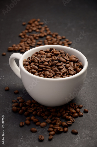 Natural organic roasted coffee beans in white cup on black background, selective focus, vertical.