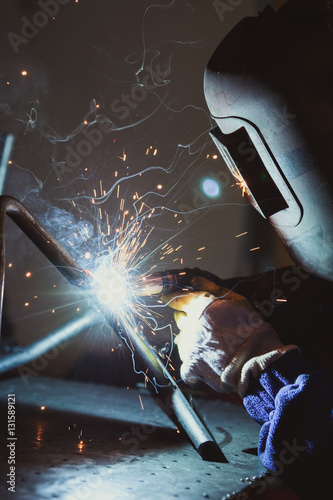 Industrial workshop man welding round pipe on a metal work table, colorful smoke, sparks and reflections