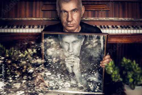 Dramatic portrait of an old grandfather with a pensive look on the background of the piano that holds the frame with his twin. He looks into the camera. Close-up portrait. Double exposure. photo