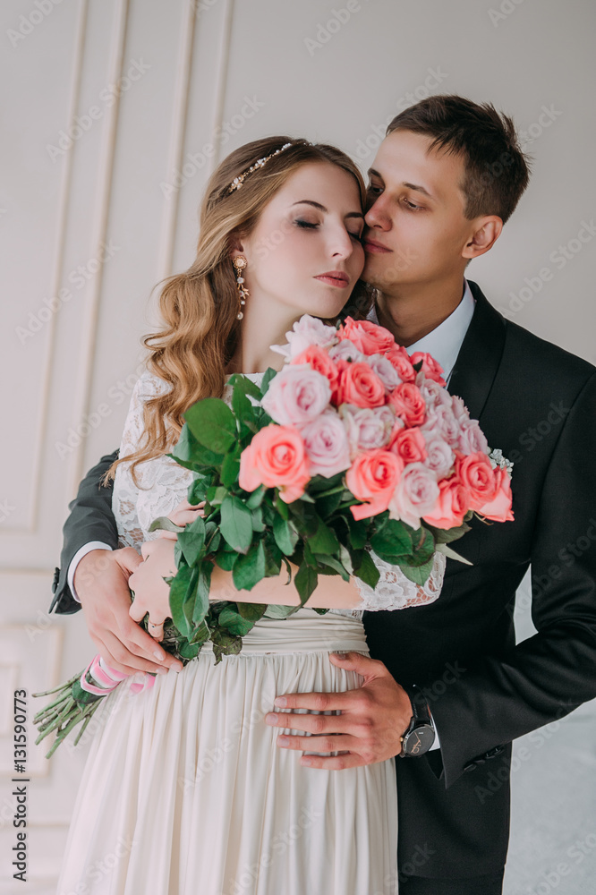 cute wedding couple in the interior of a classic white studio decorated. hey kiss and hug each other, holding hands looking at each other cute wedding couple in the interior of a classic white studio decorated. hey kiss and hug each other, holding hands looking at each other