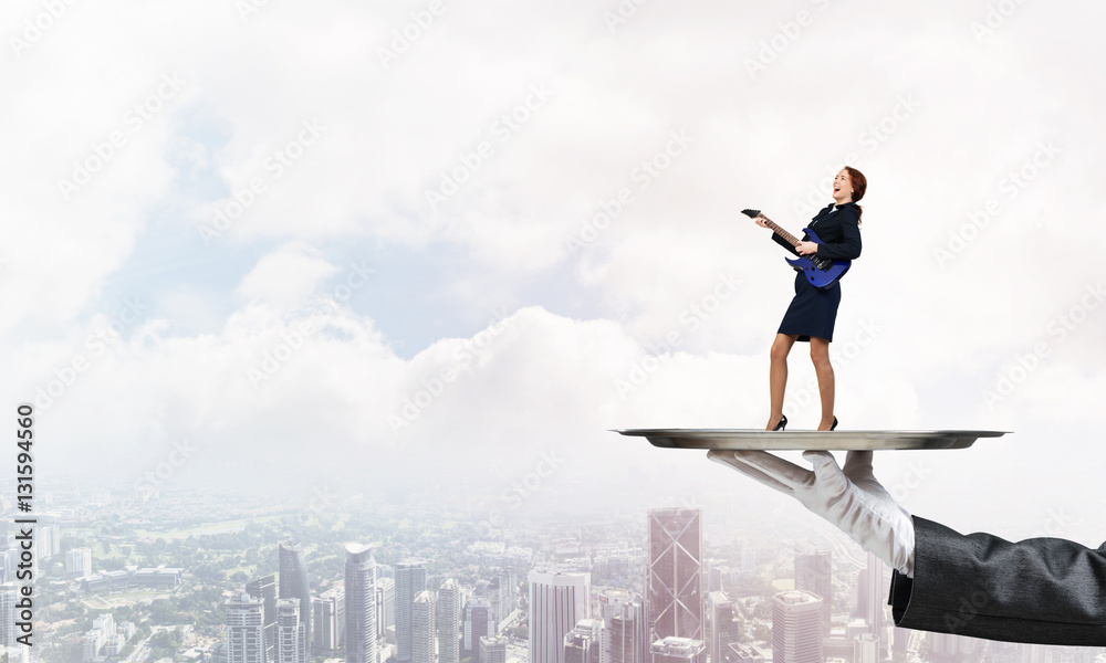 Attractive businesswoman on metal tray playing electric guitar against cityscape background Attractive businesswoman on metal tray playing electric guitar against cityscape background