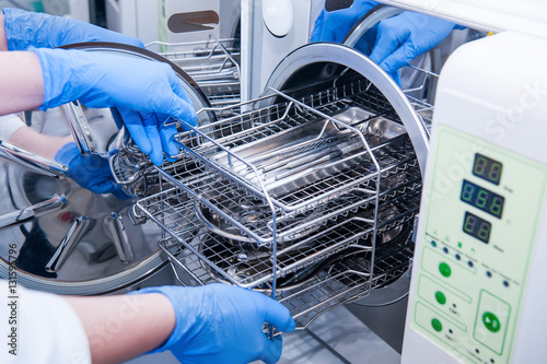 Dentist assistant's hands get out sterilizing medical instruments from autoclave. Selective focus