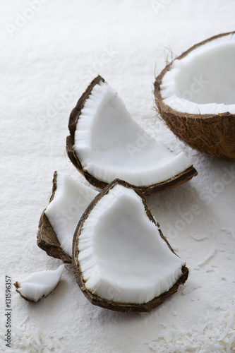 Pieces of a whole coconut cracked open on a textured white background. 