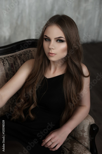 Young girl with long beautiful hair and smoky eyes wearing black maxi evening dress. Studio shot